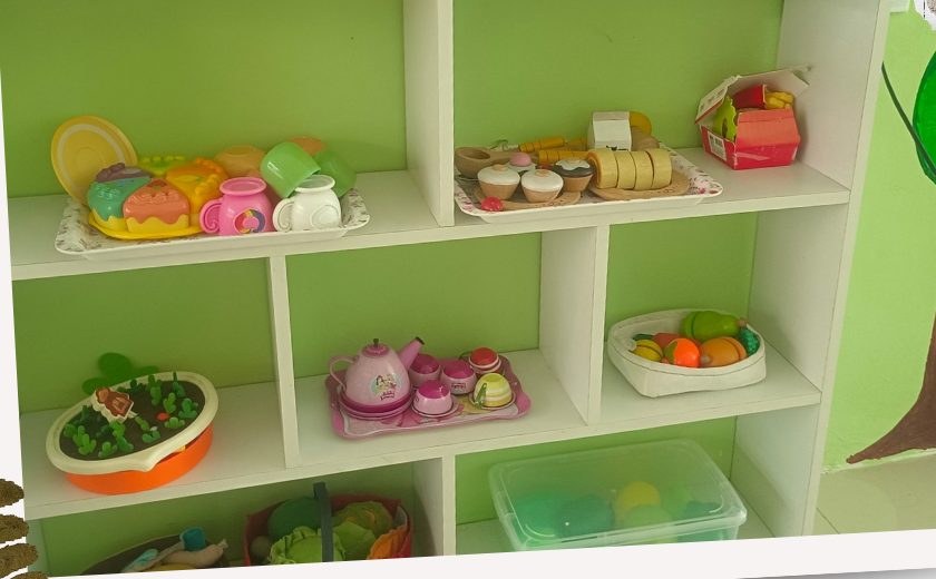 Pretend-play corner with wooden toy food and kitchen sets on low shelves
