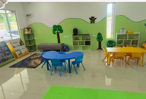 Bright, green-walled main playroom with child-size tables and reading racks