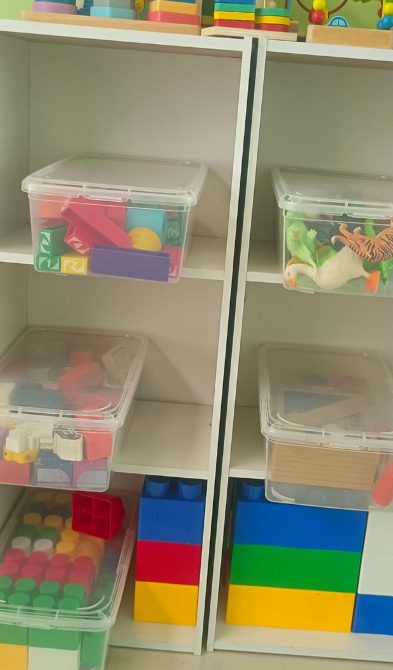 Open shelving with clear labelled bins of building blocks and learning materials